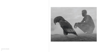 Schwarz-Weiß-Fotografie eines großen Raubvogels und eines hockenden Mannes in einer nebligen Landschaft. Der Vogel steht im Vordergrund und schaut zu Boden, der Mann im Hintergrund blickt nachdenklich zur Seite.