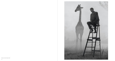 Schwarz-Weiß-Foto eines Mannes, der in einer nebligen Landschaft nachdenklich auf einer hohen Leiter sitzt. Links von ihm steht die schemenhafte Gestalt einer Giraffe.