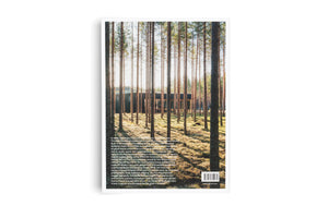 Die Rückseite eines Buches, die ein Foto eines modernen, dunklen Gebäudes in einem sonnendurchfluteten Kiefernwald zeigt. Hohe, schlanke Baumstämme stehen im Vordergrund. Der untere Teil des Covers ist mit Textblöcken und einem Barcode versehen.
