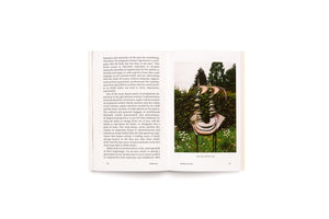 Aufgeschlagenes Buch mit Text auf der linken Seite und einem Foto auf der rechten Seite. Das Foto zeigt eine abstrakte, bronzefarbene Skulptur, die an eine Wirbelsäule erinnert und in einem Garten zwischen weißen Gänseblümchen steht. Unter dem Bild steht der Titel Mon corps de femme, 2019.