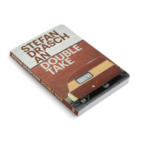 Schrägansicht des Buches Stefan Draschan Double Take. Das Coverfoto zeigt einen braun-beigen Wohnwagen vor einer roten Ziegelmauer, auf die der Titel in weißer Schrift gedruckt ist.