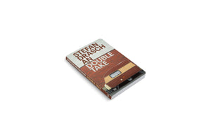Fotobuch mit dem Titel An Double Take von Stefan Draschan. Das Coverbild zeigt einen altmodischen Wohnwagen vor einer roten Backsteinmauer. Das Buch liegt auf einer weißen Fläche.