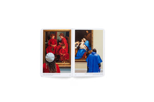 Ein aufgeschlagenes Buch zeigt zwei Fotos von Museumsbesuchern, deren Kleidung farblich zu den betrachteten Kunstwerken passt. Links trägt eine Frau in Rot vor einem Gemälde mit Mädchen in roten Kleidern. Rechts trägt eine Person einen blauen Poncho vor einem Gemälde mit einer Figur in einem blauen Gewand.