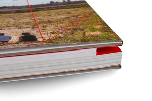 Detailaufnahme der Ecke eines dicken Hardcover-Buches auf weißem Grund. Das Cover zeigt eine Landschaftsfotografie. Aus den Seiten ragt ein roter Reiter mit der Seitenzahl 97 hervor.