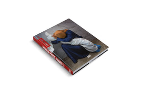 Das Hardcover-Buch World Press Photo 2024 liegt auf einem weißen Hintergrund. Auf dem Coverfoto umarmt eine Frau mit Kopftuch den in ein weißes Tuch gehüllten Körper eines Kindes.