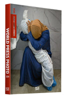 Buchcover von World Press Photo 2024, das eine trauernde Frau in einem blauen Kleid und einem Hijab zeigt, die kniend den in ein weißes Tuch gehüllten Körper eines Kindes umarmt.
