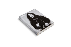 Ein graues Buch mit dem Titel Yoko Ono, Music of the Mind, liegt schräg auf einem weißen Hintergrund. Auf dem Cover befindet sich ein Schwarz-Weiß-Porträt von Yoko Ono, die einen gläsernen Hammer und eine dünne weiße Schnur in den Händen hält.