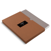 Schrägansicht eines braunen Kartonschubers mit einem schwarzen Etikett, auf dem FREQUENCIES, Oscar Murillo, VOL. 1 steht. Ein Buch mit grauem Einband ist teilweise aus dem Schuber herausgezogen.