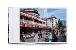 Ein offenes Fotobuch zeigt eine belebte Straßenszene in Berlin, die zwei verschiedene Epochen überlagert. Im Vordergrund ist das Café Kranzler mit rot-weißen Markisen zu sehen, vor dem Menschen aus Vergangenheit und Gegenwart flanieren. Im Hintergrund erheben sich historische Gebäude neben einem modernen Wolkenkratzer unter blauem Himmel.