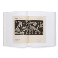 Ein aufgeschlagenes Buch mit hellgrünem Einband, das auf einer weißen Oberfläche liegt. Auf der Doppelseite ist eine schwarz-weiße Abbildung von Pablo Picassos Gemälde Guernica zu sehen, begleitet von Text in französischer und arabischer Schrift.