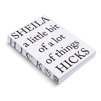 Ein weißes Buch mit dem Titel Sheila a little bit of a lot of things Hicks in schwarzer Schrift. Das Buch liegt schräg auf einer weißen Oberfläche, sodass der verzierte Buchrücken mit einem blau-schwarzen Muster sichtbar ist.