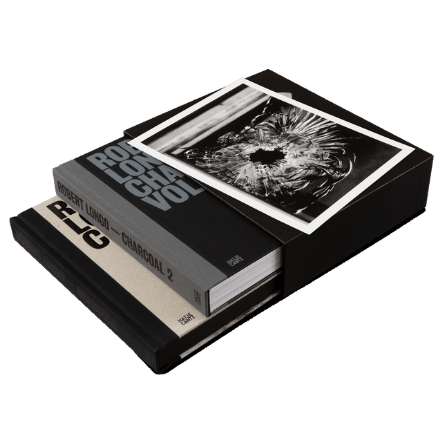 Zwei Kunstbücher von Robert Longo in einem schwarzen Schuber. Der Schuber ist mit der Schwarz-Weiß-Fotografie eines Einschusslochs in Glas versehen. Die Buchrücken mit den Titeln, darunter Robert Longo – Charcoal 2, sind sichtbar.