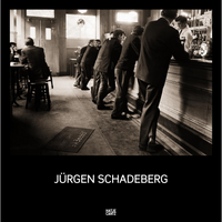 Eine Sepia-Fotografie von Jürgen Schadeberg, die eine Reihe von Männern von hinten an einer langen Theke in einer Kneipe zeigt.