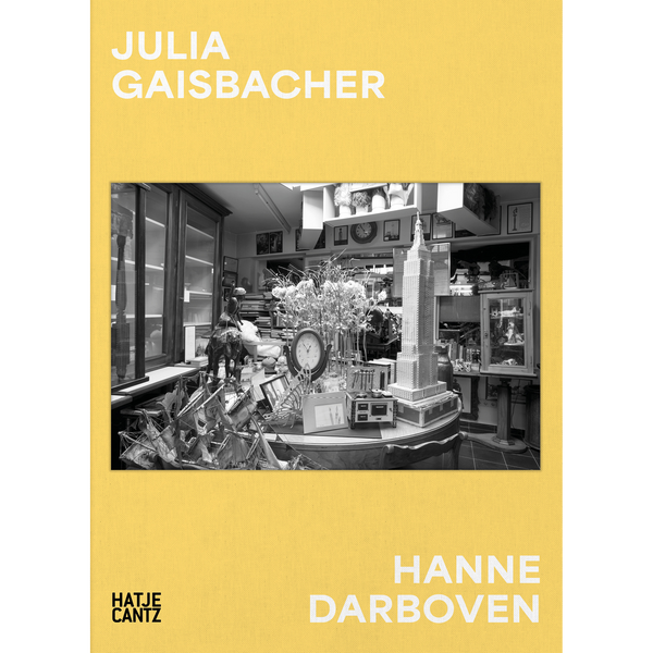 Der gelbe Bucheinband von Julia Gaisbacher und Hanne Darboven zeigt ein Schwarz-Weiß-Foto eines vollgestellten Raumes mit einem Modell des Empire State Buildings und mehreren Schiffsmodellen.