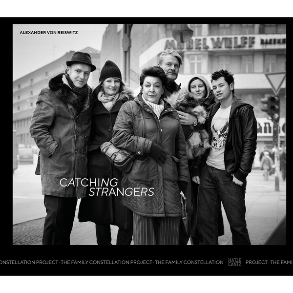 Ein Schwarz-Weiß-Foto einer Gruppe von sechs Personen und einem kleinen Hund, die auf einer Straße in der Stadt posieren. Es ist das Buchcover von Catching Strangers von Alexander von Reiswitz.