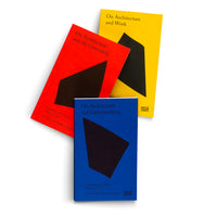 Drei Bücher mit minimalistischem Design in Blau, Rot und Gelb liegen fächerförmig auf weißem Hintergrund. Jedes Cover zeigt eine große, abstrakte schwarze Form. Die Titel lauten On Architecture and Greenwashing, On Architecture and the Greenfield und On Architecture and Work.
