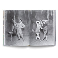 Ein aufgeschlagenes Buch zeigt eine Schwarz-Weiß-Fotografie über zwei Seiten. Links macht eine Frau einen akrobatischen Handstand, während ein Mann in gestreiftem Pullover neben ihr steht. Rechts posieren zwei Frauen in gestrickten Einteilern eng beieinander vor einem gemalten Hintergrund.
