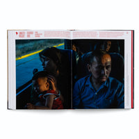 Ein aufgeschlagenes Buch zeigt eine zweiseitige Fotografie von Menschen in einem Bus. Links hält eine Frau ein Kind im Arm und blickt aus dem Fenster. Rechts sitzt ein Mann mit ernstem und müdem Gesichtsausdruck. Über und neben dem Foto befindet sich deutscher Text.
