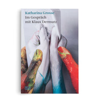 Das Buchcover von Katharina Grosse Im Gespräch mit Klaus Dermutz zeigt eine Nahaufnahme von Fingern, die mit roter, gelb-grüner und weißer Farbe verschmiert sind und ein weißes Tuch halten.