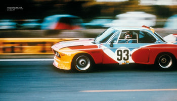 Der BMW 3.0 CSL Art Car von Alexander Calder mit der Startnummer 93 in Rot, Gelb und Hellblau fährt mit hoher Geschwindigkeit auf einer Rennstrecke, der Hintergrund ist verschwommen.