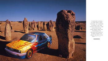 Ein buntes BMW Art Car von Ken Done steht in der sonnigen Pinnacles-Wüste in Australien. Das Auto ist mit gelben, roten und blauen abstrakten Mustern bemalt und steht zwischen hohen Felsformationen. Rechts im Bild ist ein weißer Kasten mit einem Zitat des Künstlers.