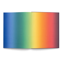 Ein aufgeschlagenes Buch auf einer weißen Oberfläche, dessen Seiten einen Regenbogen-Farbverlauf von Blau nach Rot aufweisen.