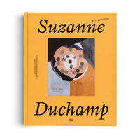 Ein gelbes Buch mit dem Titel Suzanne Duchamp Retrospective. Das Cover zeigt ein abstraktes Gemälde eines runden, schirmartigen Objekts in gedämpften Orange-, Blau- und Grautönen.