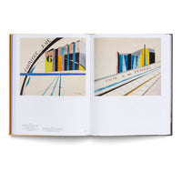 Ein aufgeschlagenes Buch, das zwei farbenfrohe, modernistische Gemälde von Fabriken zeigt. Das linke Bild trägt den Titel Fabrique de Joie, das rechte den Titel Usine de mes Pensées.