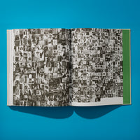 Eine Draufsicht auf ein aufgeschlagenes Buch, das auf einer leuchtend blauen Oberfläche liegt und einen dunklen Schatten wirft. Die Seiten sind mit einer dichten Collage aus Hunderten von kleinen Schwarz-Weiß-Fotografien in einem Raster gefüllt. Rechts ist ein grüner Teil des Bucheinbands zu sehen.