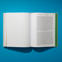Ein aufgeschlagenes Buch liegt auf einer leuchtend blauen Fläche und wirft einen dunklen Schatten, die Seiten zeigen einen englischen Text.