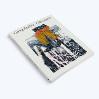 Ein weißes Buch mit dem Titel Georg Baselitz Füße zuerst liegt schräg auf einer weißen Oberfläche. Das Cover zeigt ein expressionistisches Gemälde einer auf dem Kopf stehenden Figur mit gelber Hose und schwarzen Stiefeln.